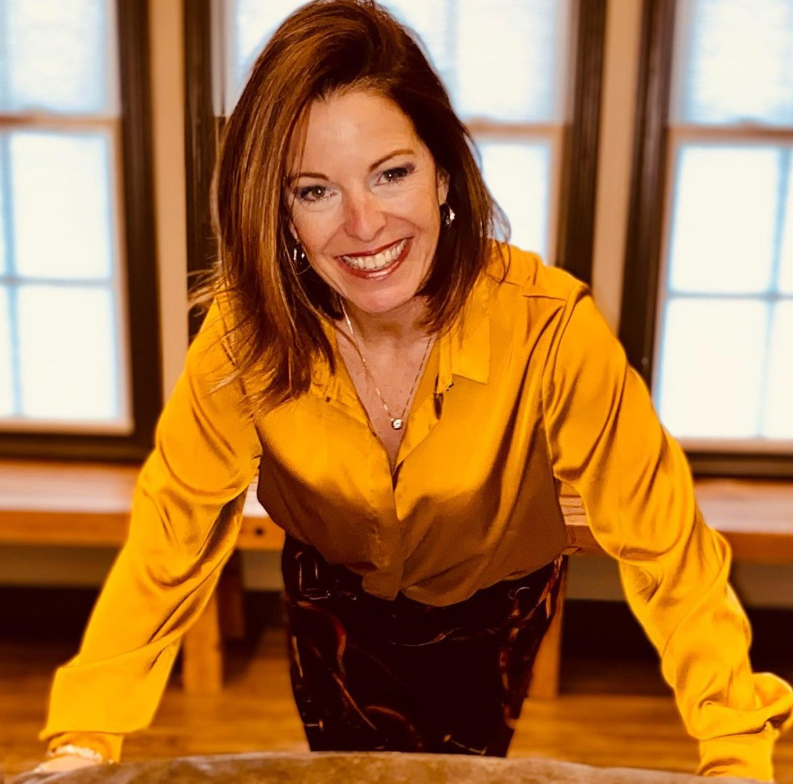 Portrait of Jessica Ashe, Minister of Foreign Affairs for the Kingdom of Hawaiʻi, smiling in a golden blouse, representing diplomacy and international relations.