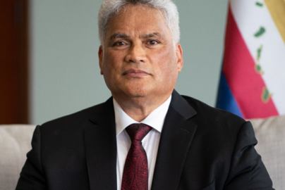 King Edmund Keliʻi Paki-Silva Jr. seated in a suit and tie with the Hawaiian flag in the background, representing his role as Sovereign of the Kingdom of Hawaiʻi.