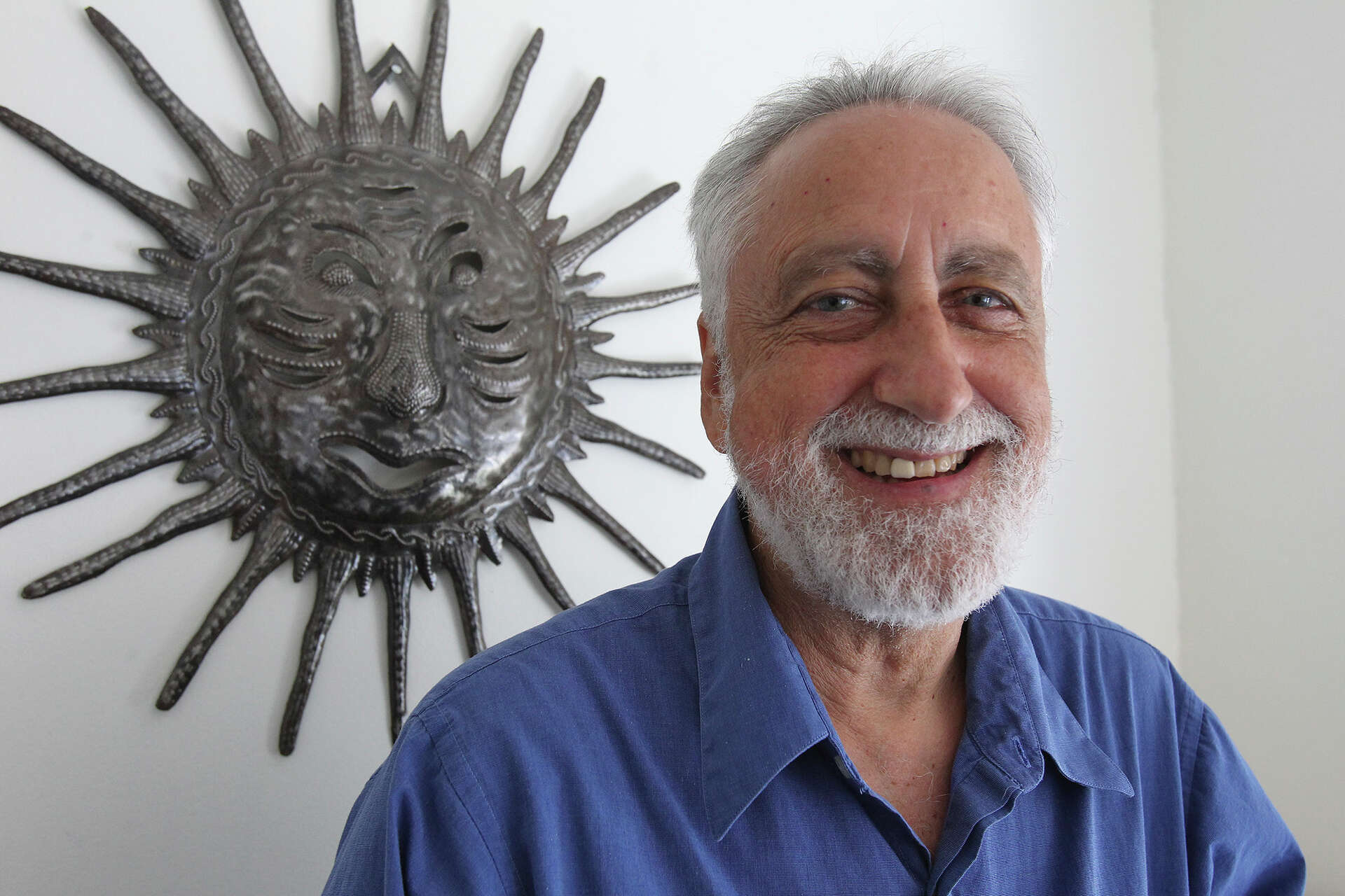 Portrait of Lanny Sinkin, Aliʻi Manaʻo Nui (Chief Advisor) of the Kingdom of Hawaiʻi, smiling in front of a sun sculpture, symbolizing wisdom and guidance.
